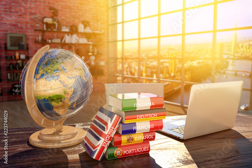 Languages learning and translate, communication and travel concept, books with covers in colors of flags of Europe countries, laptop and globe on a table in a modern interior photo