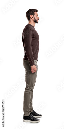 A bearded man in casual clothes stands still with arms hanging straight on his sides in a side view.