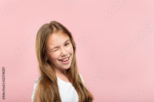 emotion face. smiling cute adolescent girl pleased with herself. young pretty brown haired kid winking. portrait on pink background.