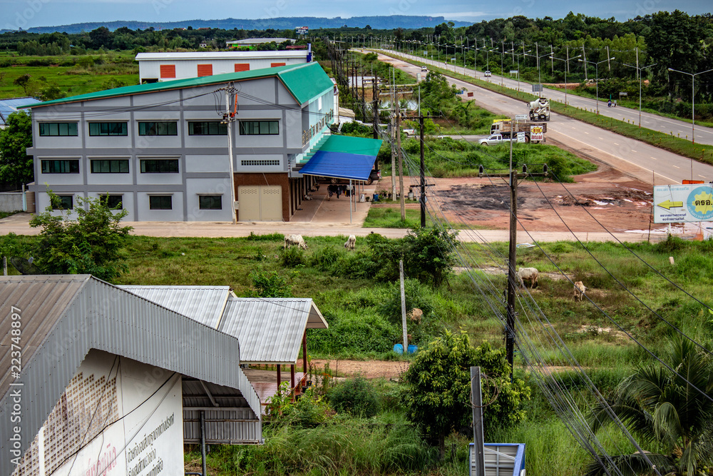 Looking down on some buildings and grass in Bueng Kan Thailand. A highway is visible running into a mountain range on the distance.