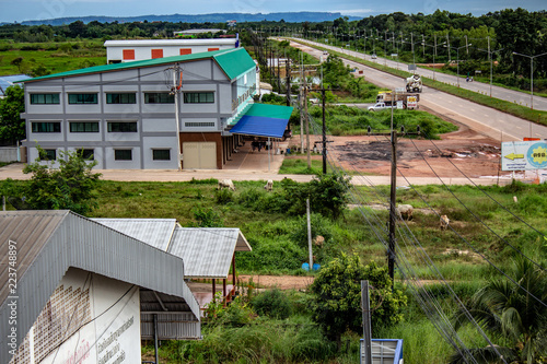 Obraz na płótnie Looking down on some buildings and grass in Bueng Kan Thailand. A highway is visible running into a mountain range on the distance. w salonie