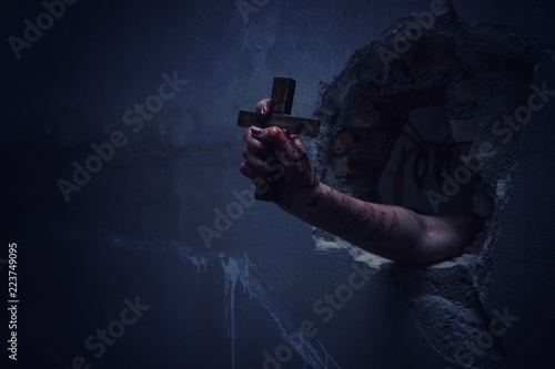 Horror Scene with Bloody Hand is holding a holy cross.