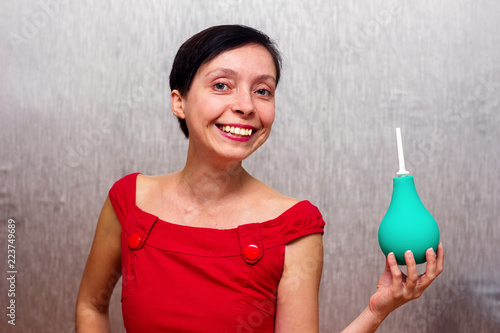 Smiling and happy woman holding an enema isolated by gray background. photo