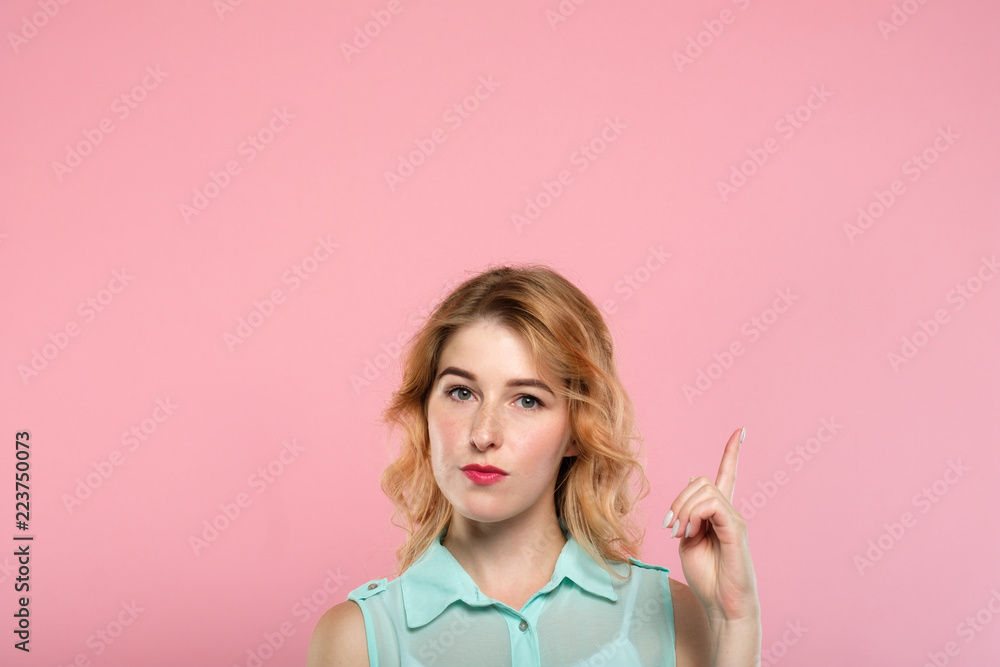 look up. beautiful blond girl pointing upward with her index finger turning attention to a virtual object or text bubble. empty space for advertising. portrait of a cute blond on pink background. look up. beautiful blond girl pointing upward with her index finger turning attention to a virtual object or text bubble. empty space for advertising. portrait of a cute blond on pink background.