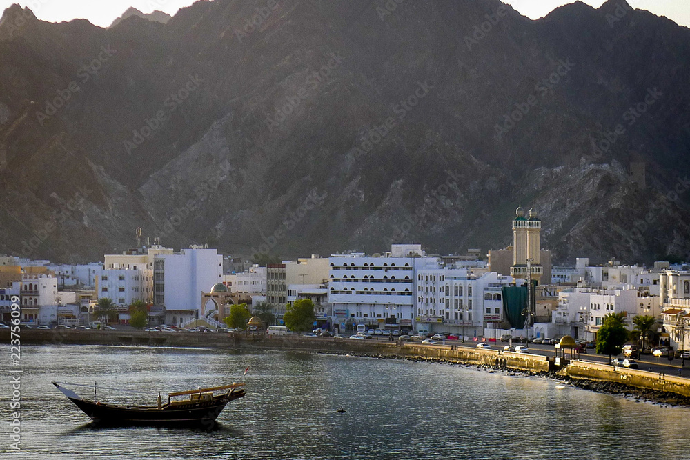 MUSCAT, OMAN - Jan 2012: A dhow boat floats in the harbour in front of the spectacular corniche at Mutrah, the former commercial center of Muscat, lined with whitewashed buildings and minarets