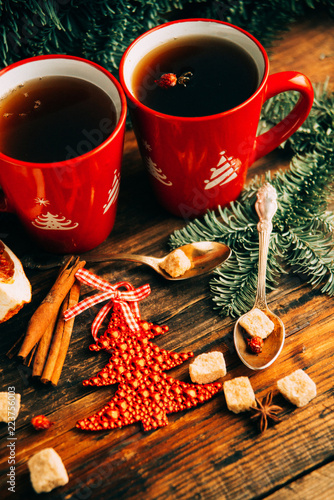 Close-up two glass cups full of hot, red, aromatic lemon tea with dark chocolate on a pine branch and table background. Winter snacks composition.