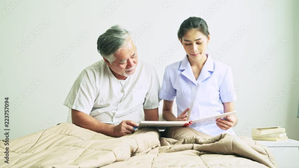 Young beautiful female nurse reading book to senior man. Asian woman reading book to old asian man with white beard in bed. Senior home service, care taker concept.