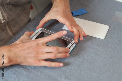 Preparing the phone to replace the screen concept. High angle top view cropped photo man is holding a new protective 3D glass over the smartphone