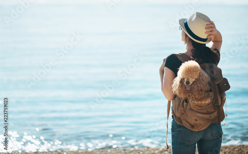 Woman traveler with dog in the backpack and looking at sea. Concept of travel.