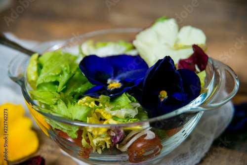 Spring vitamin salad: greens with cherry tomatoes and edible flowers (pansies) on a natural wood background. The concept of healthy eating. photo