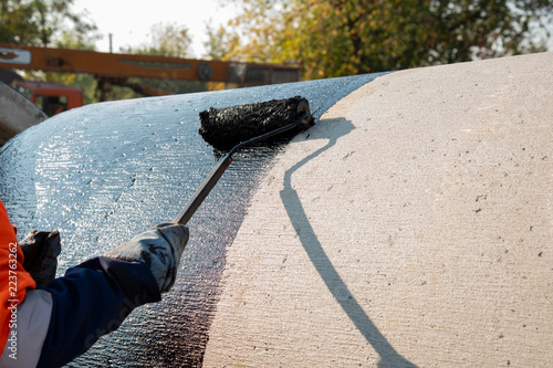 Foto Roofer worker painting black coal tar or bitumen at concrete