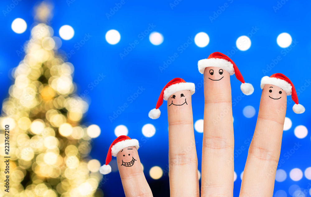 Naklejka premium holidays and body parts concept - close up of four fingers with santa hats over christmas tree lights background