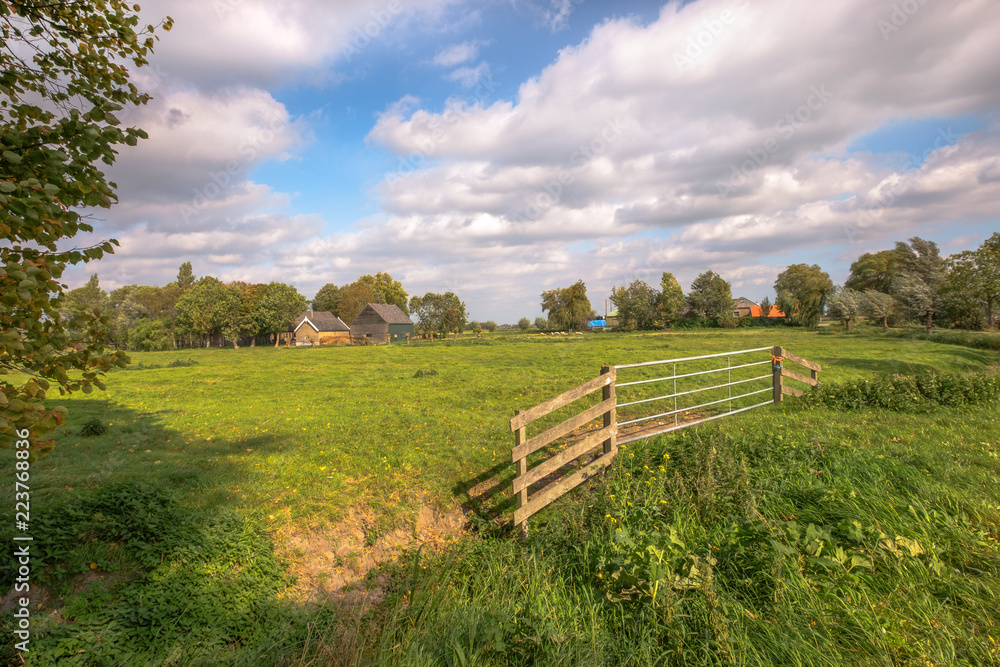 A large fence for a beautiful green meadow of a farm with a beautiful cloudy sky.