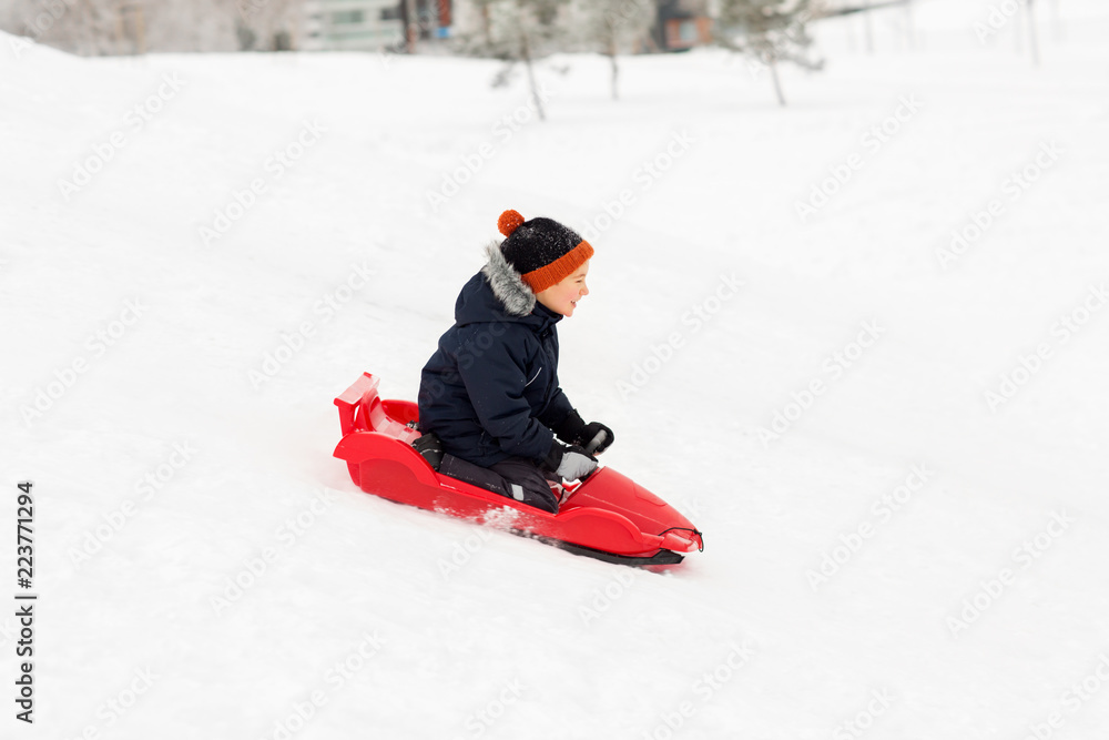childhood, sledging and season concept - happy little boy sliding on sled down snow hill outdoors in winter childhood, sledging and season concept - happy little boy sliding on sled down snow hill outdoors in winter