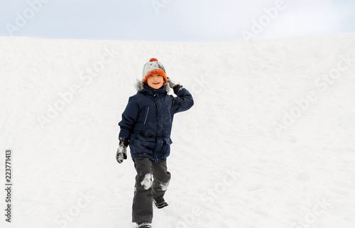 childhood, leisure and season concept - happy little boy throwing snowball in winter