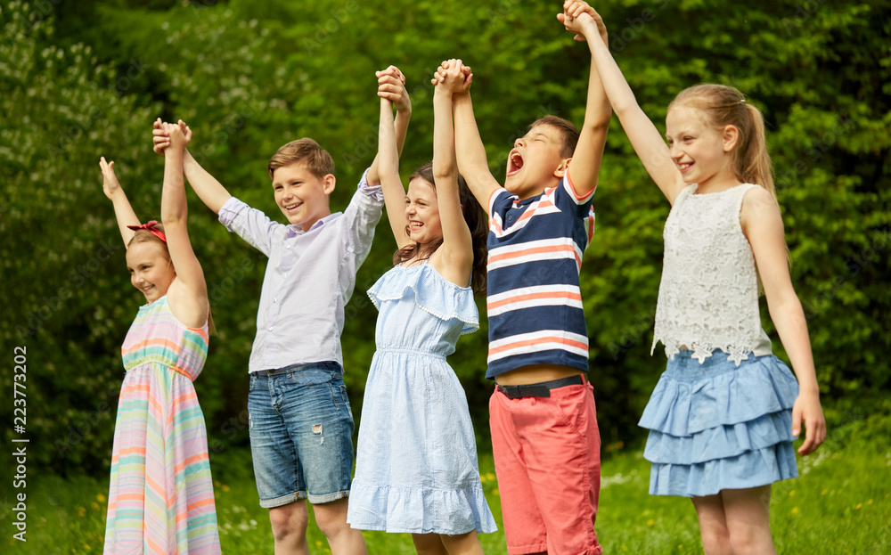 Obraz premium childhood and friendship concept - happy kids holding raised hands in summer park