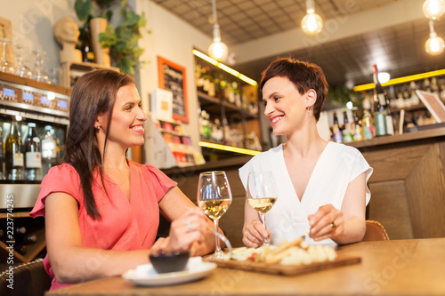 leisure, people and lifestyle concept - happy women eating snacks at wine bar or restaurant