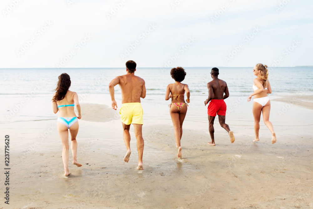 friendship, summer holidays and people concept - happy friends running on beach