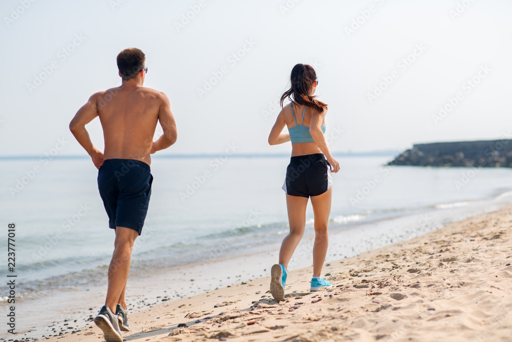 fitness, sport and lifestyle concept - happy couple running along summer beach fitness, sport and lifestyle concept - happy couple running along summer beach