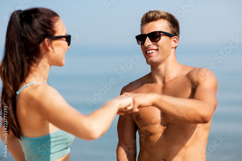 fitness, sport and lifestyle concept - happy couple in sports clothes and sunglasses on beach making fist bump gesture