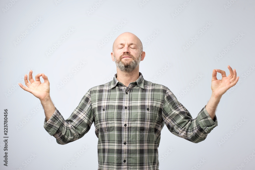Naklejka premium Yoga and meditation concept. Handsome bald man with bristle keeping eyes closed while meditating