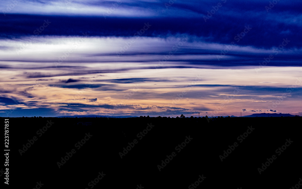 A beautiful and colourful sunset in Bueng Kan City, Thailand showing the skyline of mountains, trees and spotted structures.