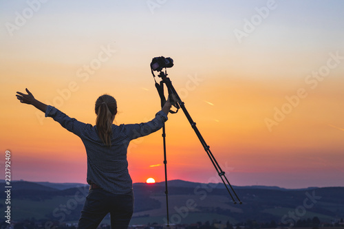 Enjoying spending time with camera in nature. Photographer holding a tripod and looking at sunset. 