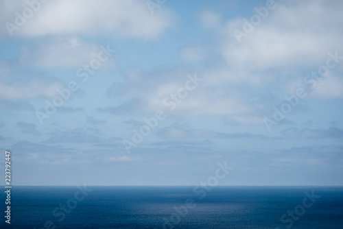 Low ocean horizon below fluffy clouds and blue sky.