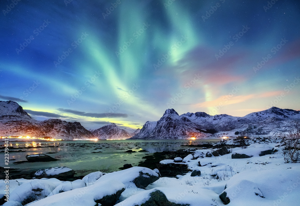 Fototapeta premium Aurora borealis on the Lofoten islands, Norway. Green northern lights above mountains. Night sky with polar lights. Night winter landscape with aurora and reflection on the water surface. 