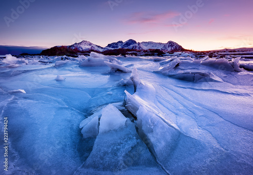 Fototapeta samoprzylepna Grzbiet górski i odbicie na zamarzniętej powierzchni jeziora. Naturalny krajobraz na Lofotach w Norwegii. Woda i góry podczas zmierzchu.