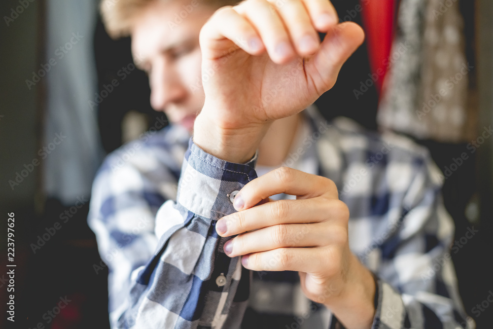 close up young man put on casual shirt at home, adjusting a button an the sleeve close up f