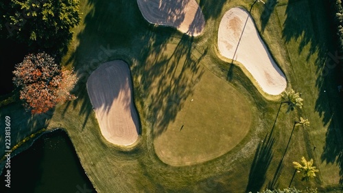 aerial image of a golf field course with a flag and hole and some sand and water pools with beautiful grass
