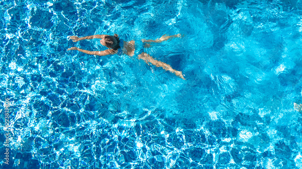 Aerial drone view of active girl in swimming pool from above, yong woman swims in blue water, tropical vacation, holiday on resort concept
