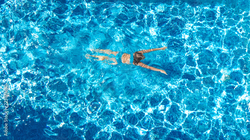 Aerial drone view of active girl in swimming pool from above  yong woman swims in blue water  tropical vacation  holiday on resort concept  