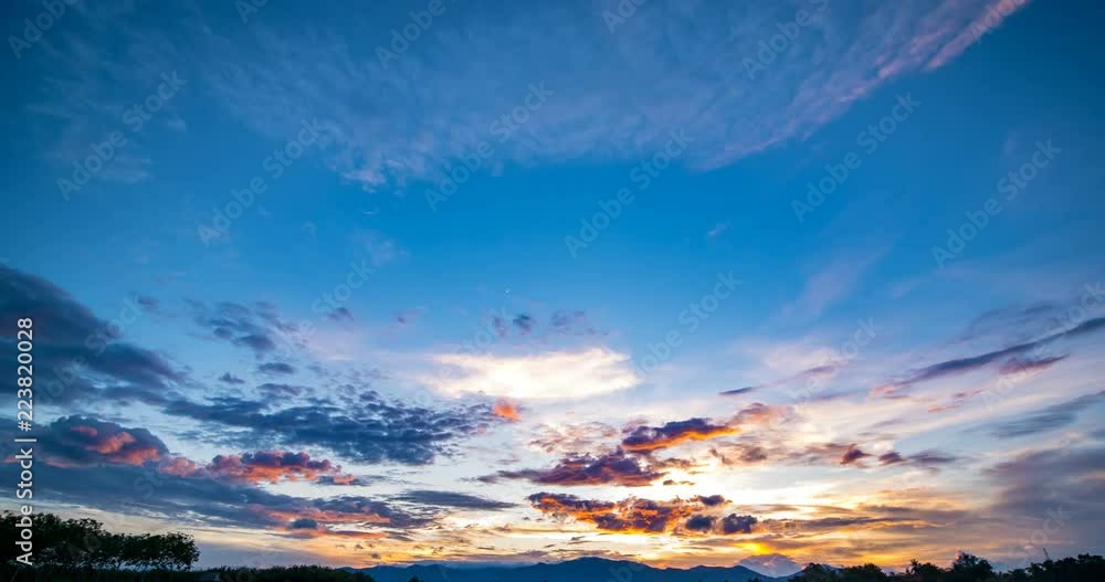 Day to night with sunset behind overcast sky over field with view of mountain in background