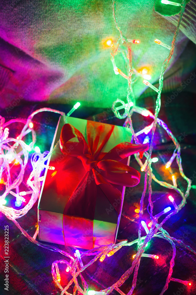 gift box with red satin bow on a shiny garland background gift box with red satin bow on a shiny garland background