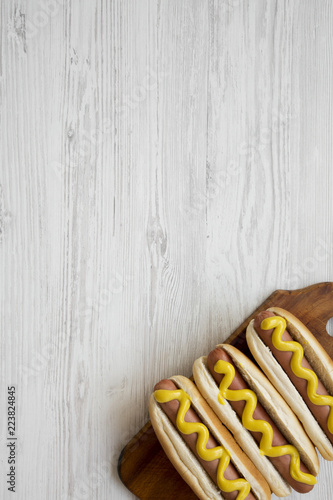 Hot dog with yellow mustard on wooden board on white wooden background, top view. Copy space.