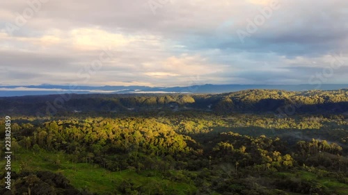 Aerial view over the Ecuadorian Amazon with the first rays of sun illuminating the rainforest at dawn, pan to distant Sumaco Volcano partially concealed in the clouds.