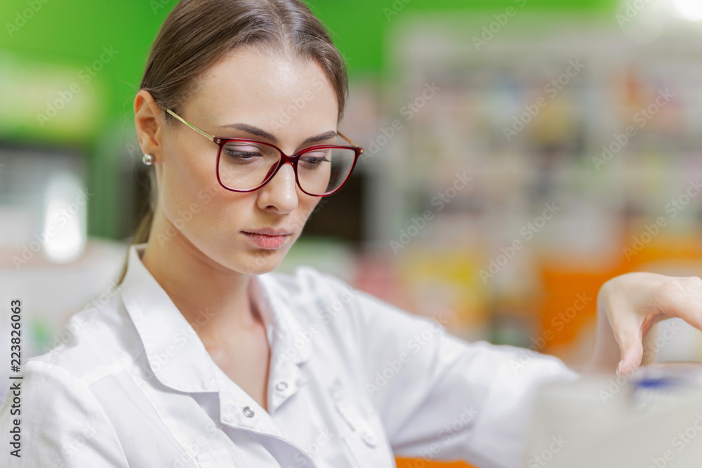 A pretty graceful dark-haired lady with glasses, dressed in a white coat, carefully examies the goods on the shelf in the pharmacy. A pretty graceful dark-haired lady with glasses, dressed in a white coat, carefully examies the goods on the shelf in the pharmacy.