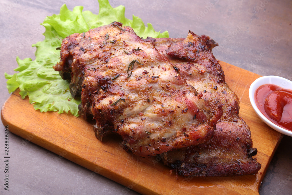 grilled barbecued ribs with lettuce leaves, hot chili pepper and sauce on wooden cutting board. grilled barbecued ribs with lettuce leaves, hot chili pepper and sauce on wooden cutting board.