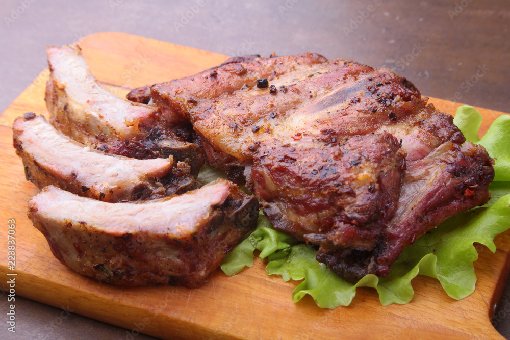 grilled barbecued ribs with lettuce leaves, hot chili pepper and sauce on wooden cutting board.