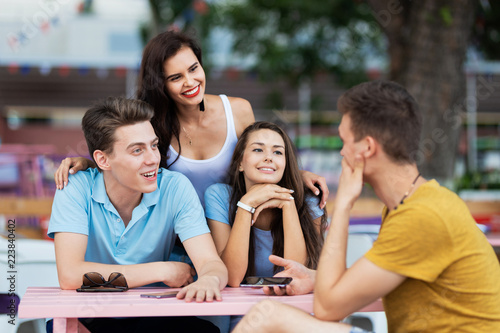 A company of good-looking friends is laughing, socialising and sitting at the table in the nice summer cafe. Entertainment, having good time. Friendship.
