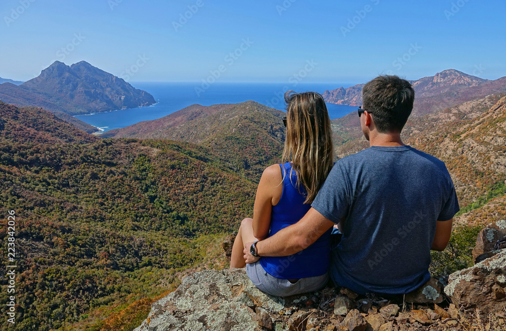 Naklejka premium CLOSE UP: Unrecognizable couple sitting on rocky ledge overlooking the seaside.