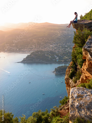 AERIAL: Young woman sitting on the edge of a cliff above the stunning seaside.