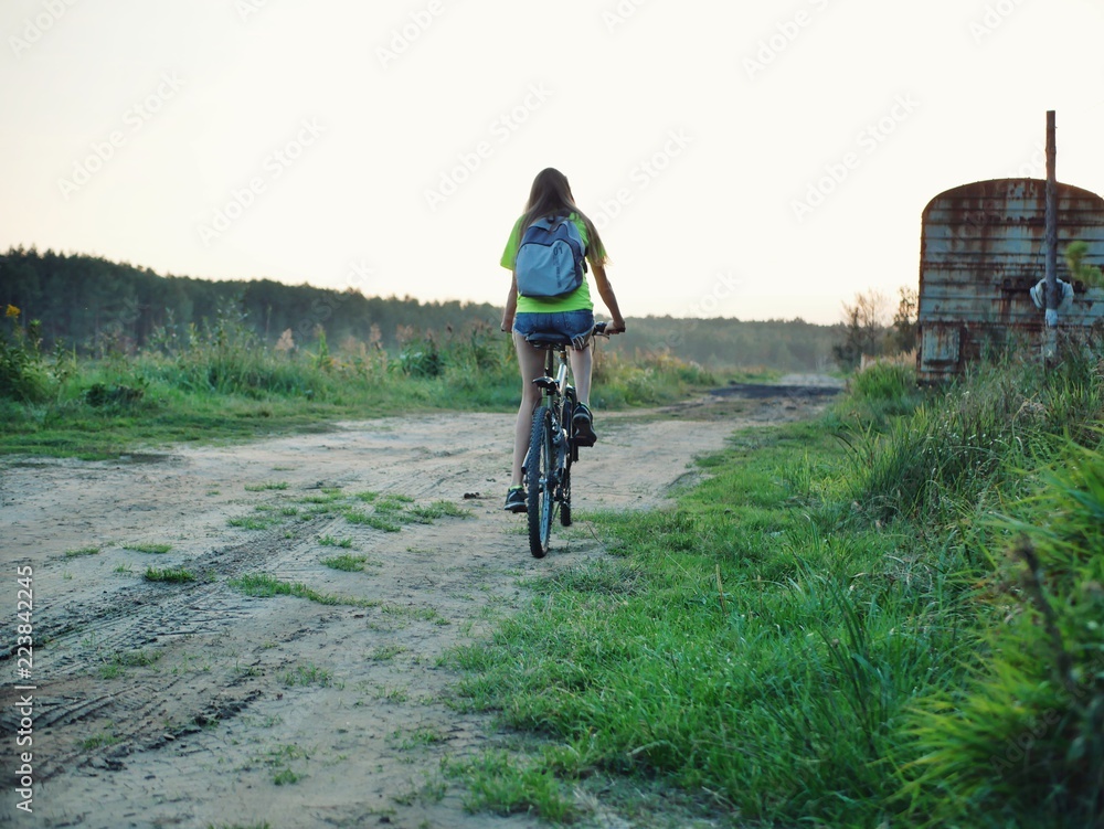 Polonne / Ukraine - 14 September 2018: girl in a green T-shirt with a backpack riding a bike Polonne / Ukraine - 14 September 2018: girl in a green T-shirt with a backpack riding a bike