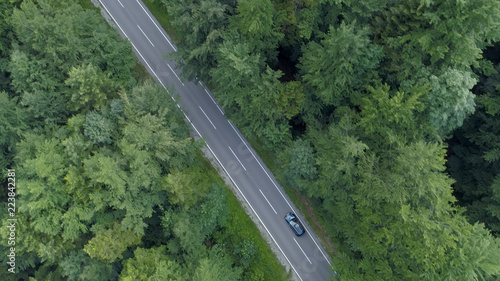 AERIAL: Dark colored tourist car driving down empty asphalt road in the forest.
