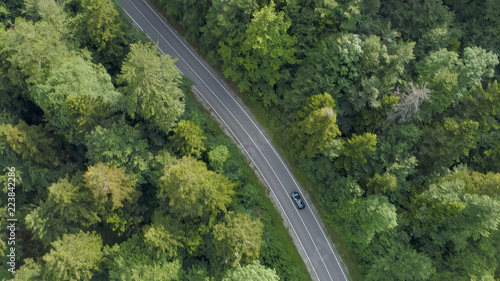 AERIAL: Flying above a car cruising along a country road running through forest.