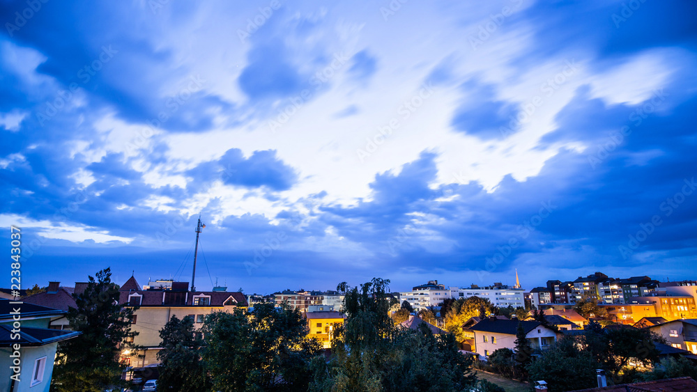 Wide shot of late evening partly cloudy sky with city lights bellow