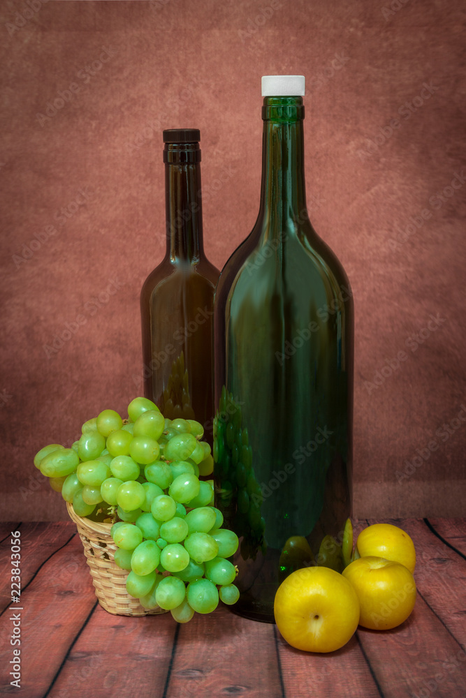 still life of two bottles, grapes and yellow plums on a red background