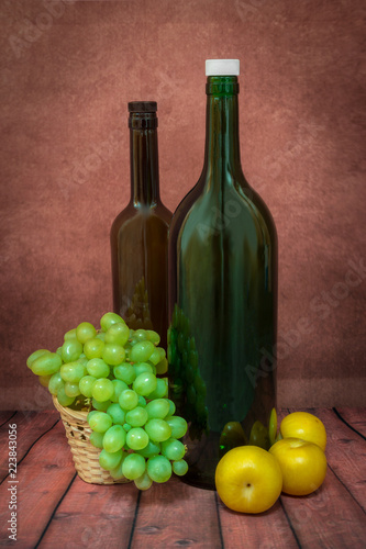 still life of two bottles, grapes and yellow plums on a red background